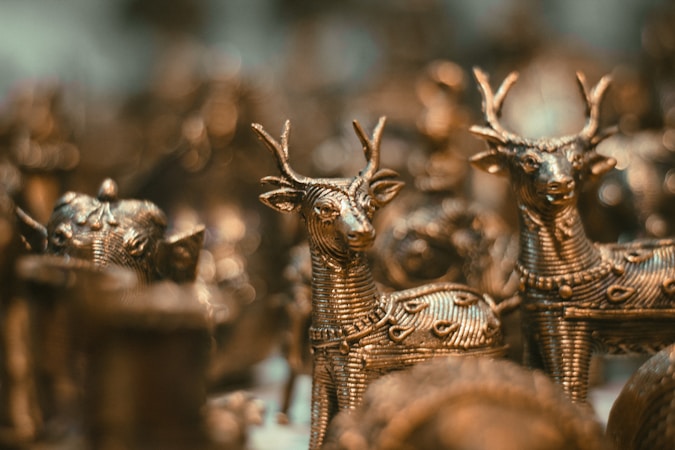 Intricately designed metal figurines of deer are closely arranged, showcasing detailed craftsmanship with textured patterns on their bodies. The focus is on the elegant forms and antlers of the deer, with a soft bokeh effect creating a warm ambiance in the background.