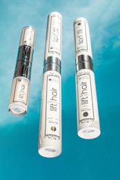 Three bottles of beauty products with silver accents are arranged on a bright blue background. The labels read 'lift hair' with various product names including shampoo and soin. The overall design is clean and modern.