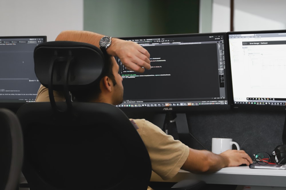 um homem sentado na frente de dois monitores de computador