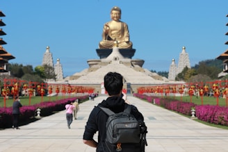 a man with a backpack looking at a large buddha statue