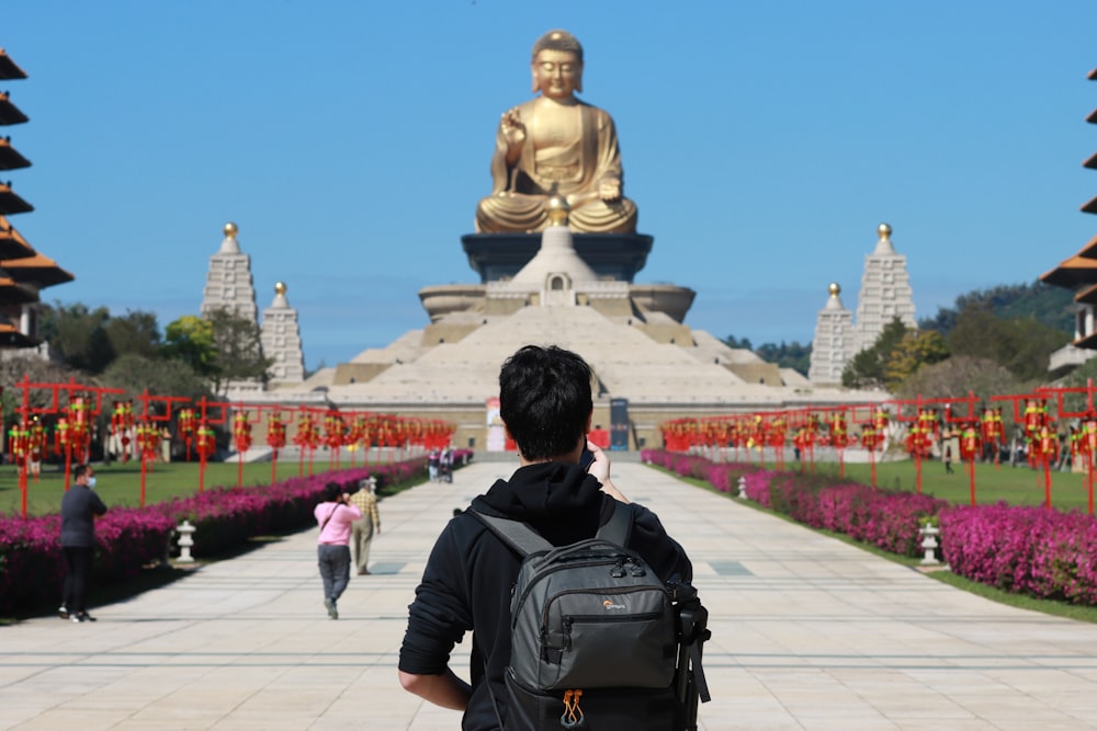 a man with a backpack looking at a large buddha statue