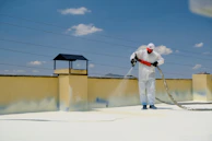 a man in a white coverall spray painting a roof
