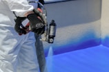 a man in white coveralls painting a wall with blue paint