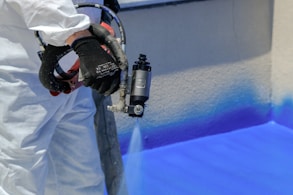 a man in white coveralls painting a wall with blue paint