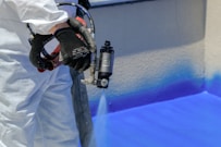 a man in white coveralls painting a wall with blue paint