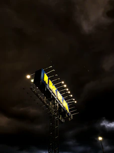 A towering billboard illuminated against the evening sky on a bustling highway.