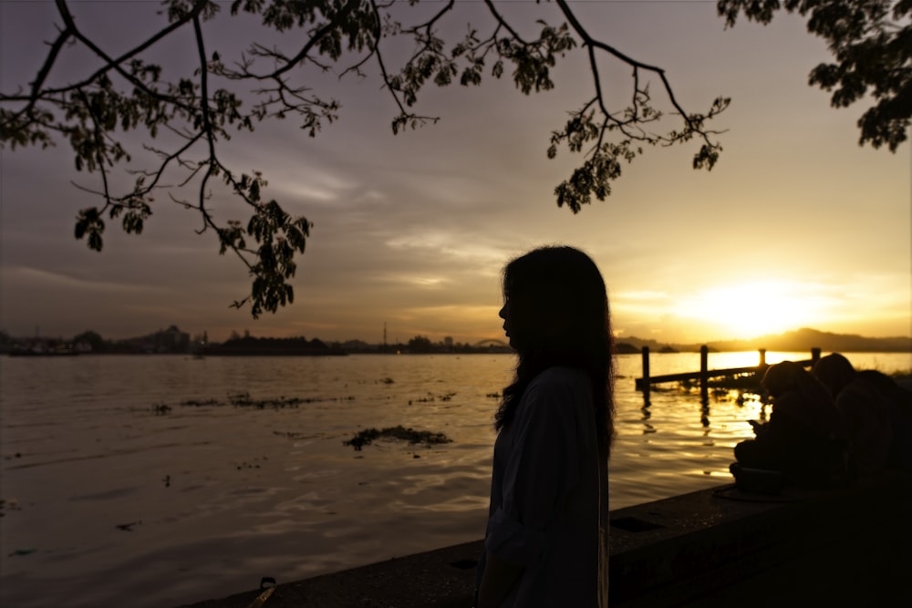 a woman standing next to a body of water at sunset