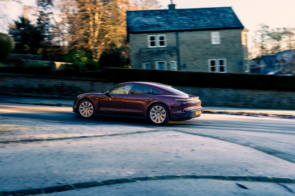 a purple car driving down a street next to a house