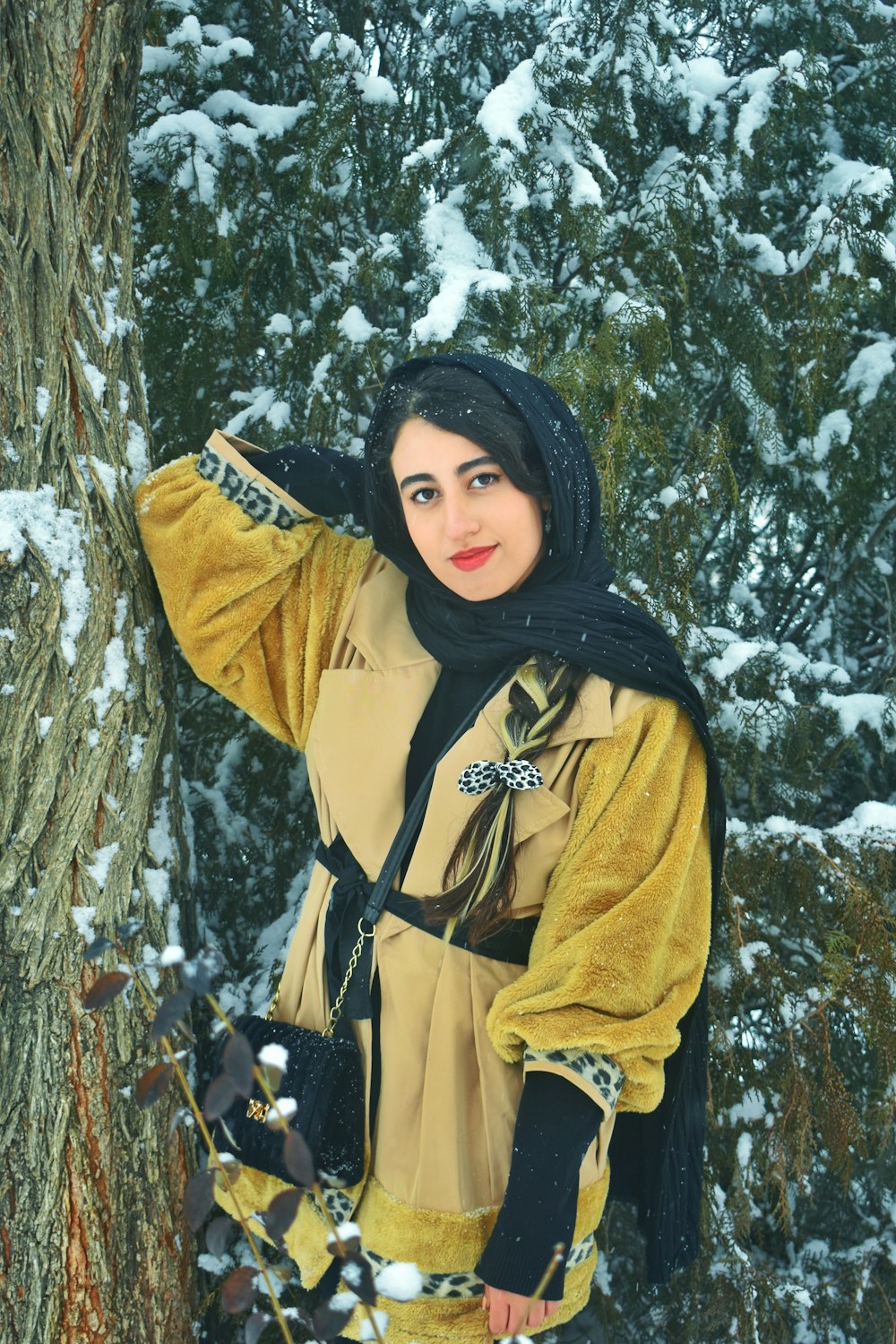 a woman standing next to a tree in the snow