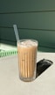 Refreshing iced coffee with ice cubes and a straw in a clear glass, set against a bright orange background.