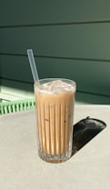 Refreshing iced coffee with ice cubes and a straw in a clear glass, set against a bright orange background.