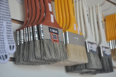 A row of paintbrushes with various sizes and colored handles hangs neatly in a display, showcasing both natural and synthetic bristles. The arrangement is organized, suggesting a retail or hardware store setting.