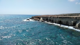 a rocky cliff overlooks the ocean with clear blue water