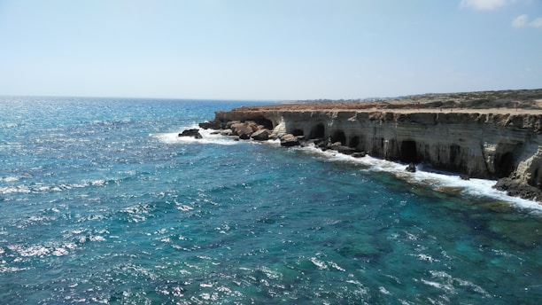 a rocky cliff overlooks the ocean with clear blue water