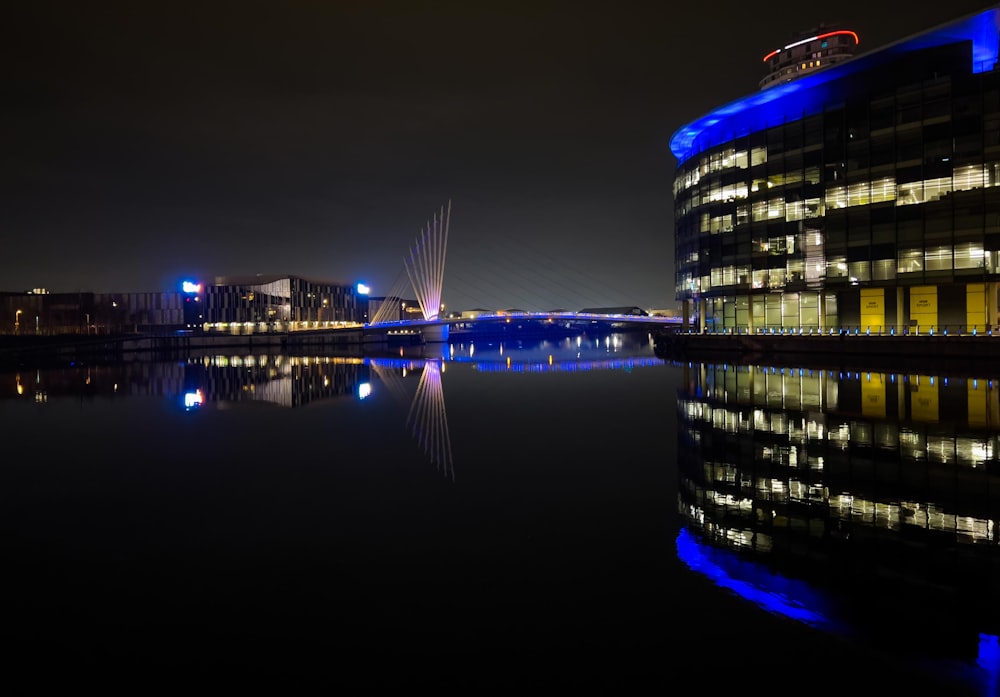 a building is lit up at night next to a body of water