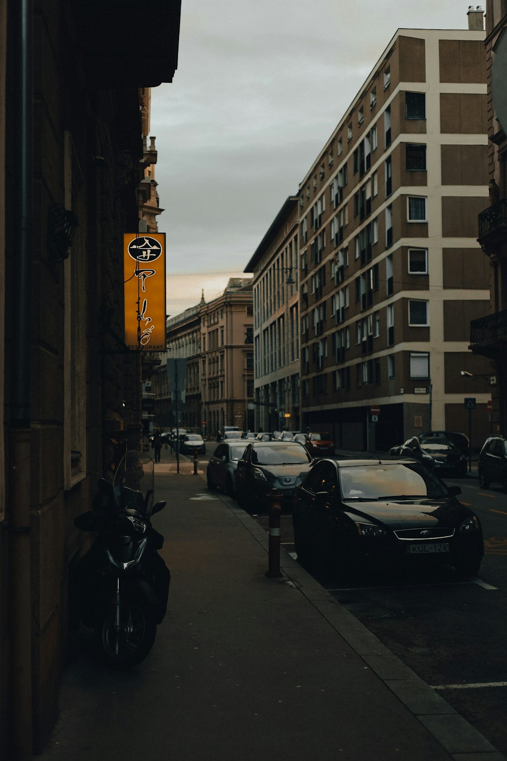 a city street lined with parked cars next to tall buildings