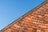 A section of a red brick roof is captured against a clear blue sky. The roof tiles are arranged in a neat, overlapping pattern, creating a textured and orderly geometric design.