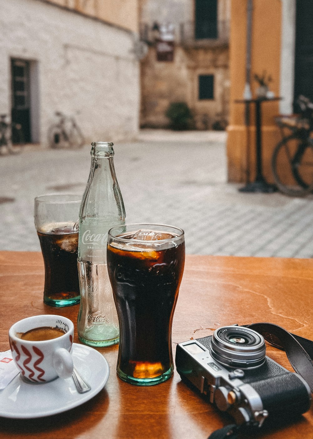 a camera, a cup of coffee, and a bottle of soda on a table