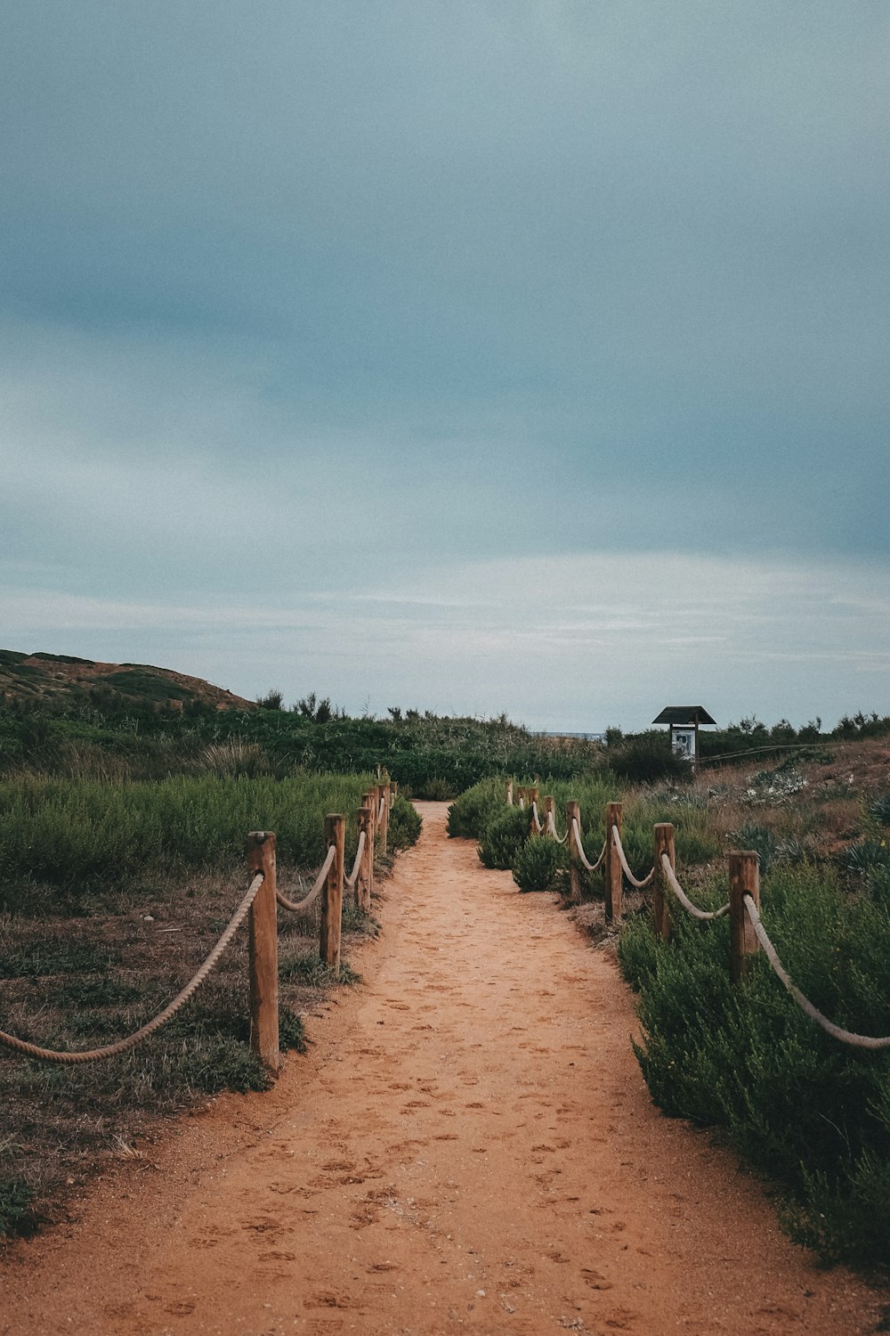 a dirt path with a fence and a house in the distance