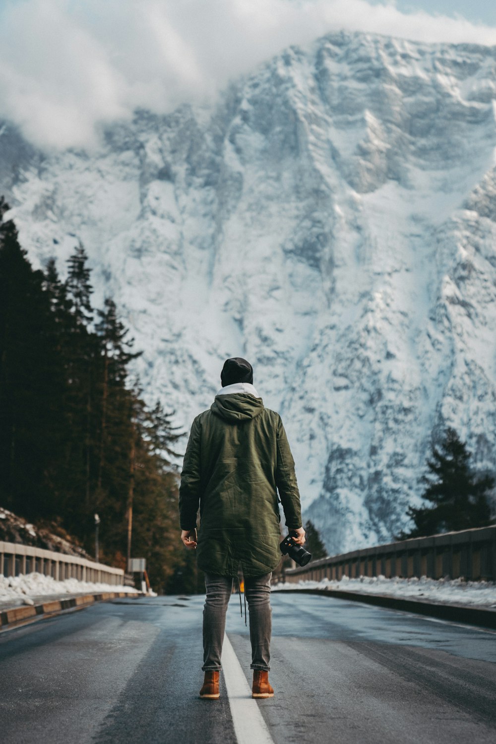 a man walking down a road in front of a snow covered mountain