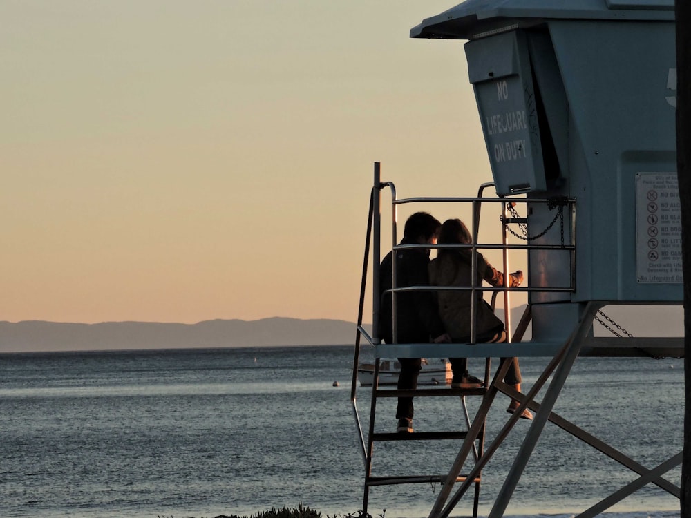 Zwei Personen sitzen auf einem Rettungsschwimmerturm mit Blick auf den Ozean