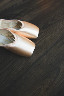 Close-up of ballet slippers on a polished wooden floor with golden accents.