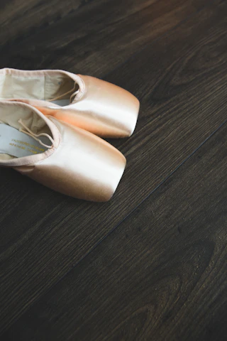 Close-up of ballet shoes on polished wooden floor with delicate shadows.