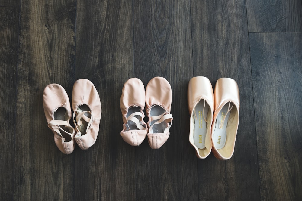 three pairs of ballet shoes lined up on a wooden floor