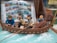 A group of animated characters is depicted in a small boat surrounded by water with foam effects. They appear to be involved in a nautical adventure, with some characters holding oars. The backdrop includes an open comic book with scenes and dialogues related to the adventure.