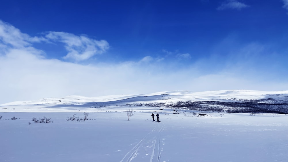 a couple of people walking across a snow covered field