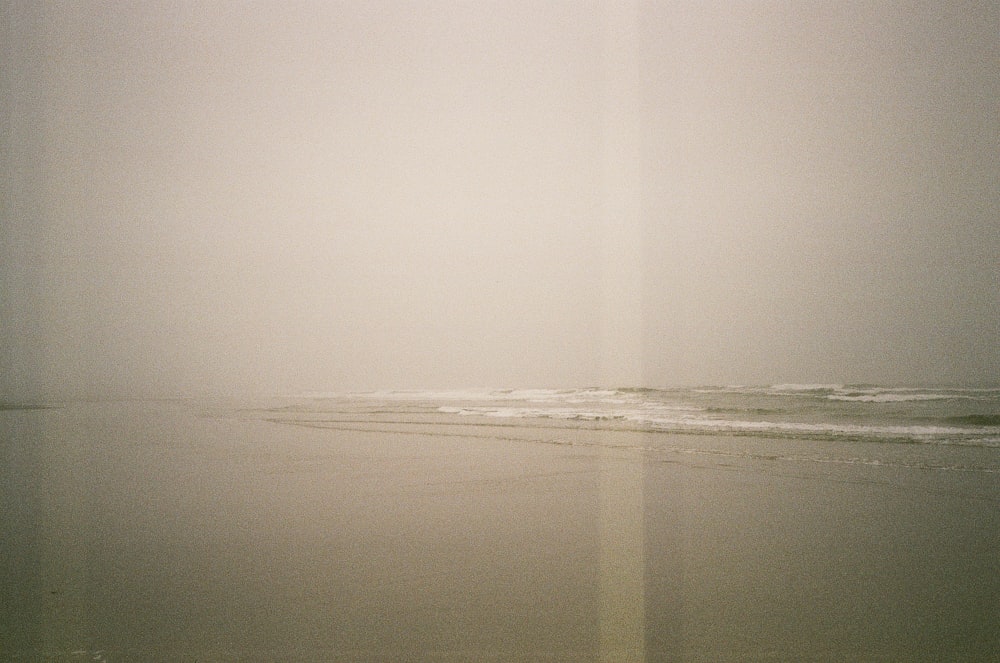 a foggy day at the beach with a lone surfer