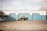A vintage pickup truck is parked in front of a blue and white automotive shop called Master Muffler. The building has large, closed garage doors and signage that includes services like catalytic converters, brakes, shocks, and struts. The sky is partly cloudy, and there are no people present.
