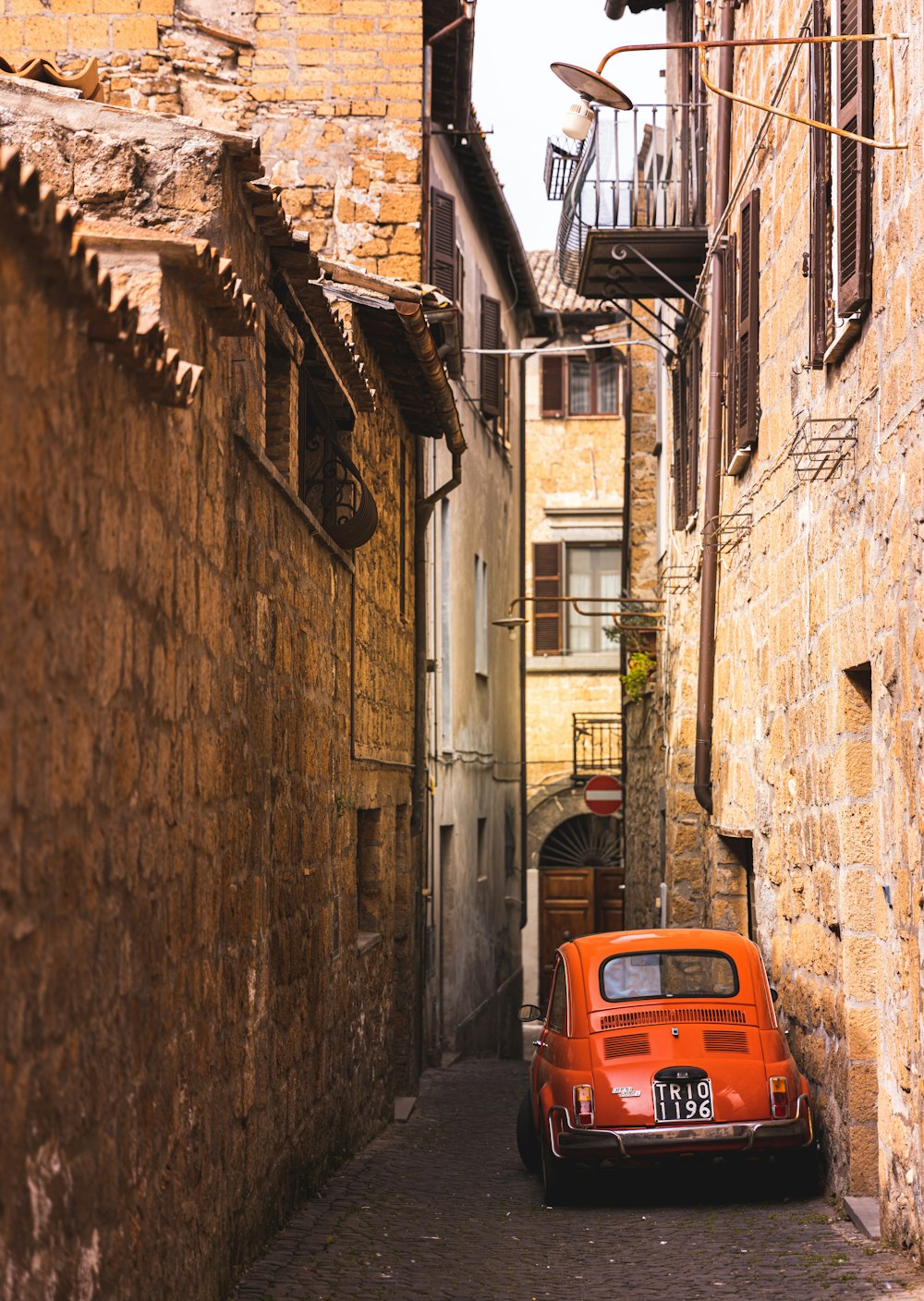 an orange car parked in a narrow alley way