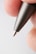 A close-up view of the tip of a metallic pen held between two fingers, with visible fingerprint details.