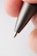 A close-up view of the tip of a metallic pen held between two fingers, with visible fingerprint details.
