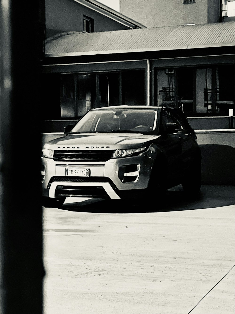 a black and white photo of a car parked in front of a house