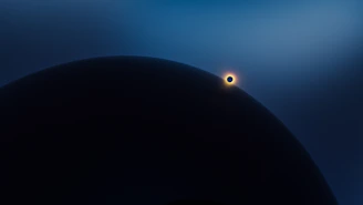 A large celestial body is partially obscured by shadow in the foreground, with a smaller, illuminated body positioned nearby, emitting a halo of light against a gradient blue sky.