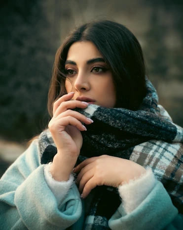 A candid moment of a woman smiling softly, wrapped in a warm scarf during a chilly morning.