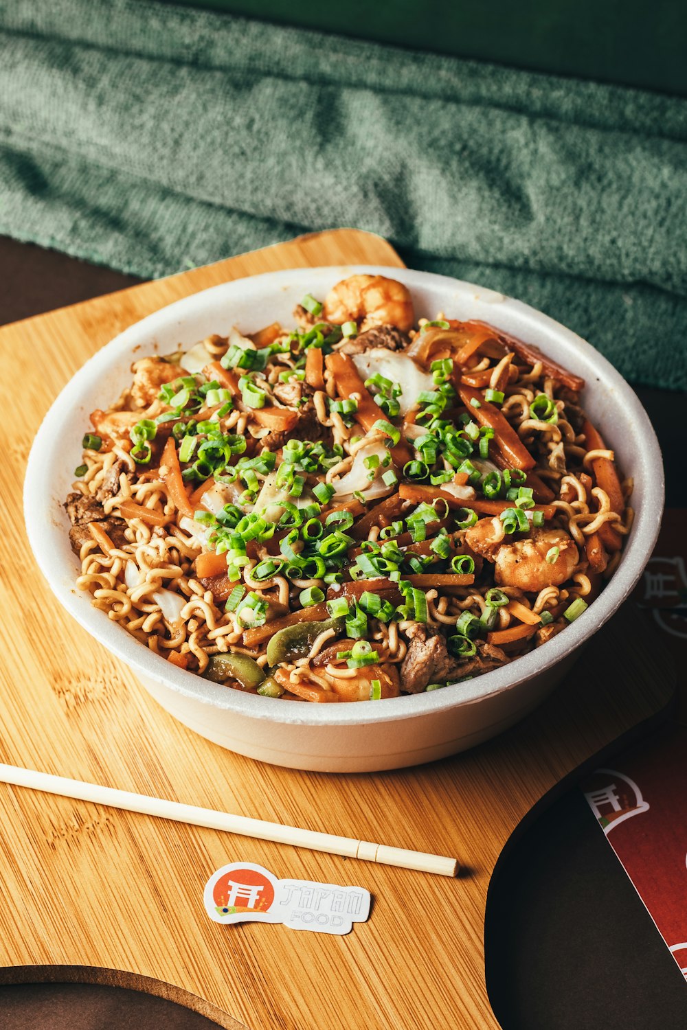 a bowl of noodles and vegetables on a cutting board