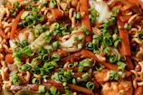 Close-up of steaming hot wok noodles with colorful vegetables and tender chicken pieces.