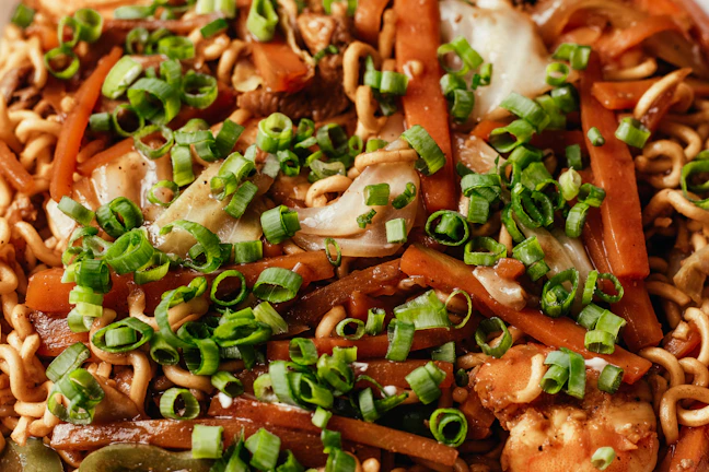 Close-up of steaming hot wok noodles with colorful vegetables and tender chicken pieces.