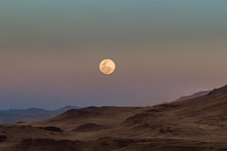 a full moon rising over a desert landscape