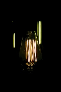 An illuminated Edison-style light bulb with visible filaments glowing warmly against a dark background.