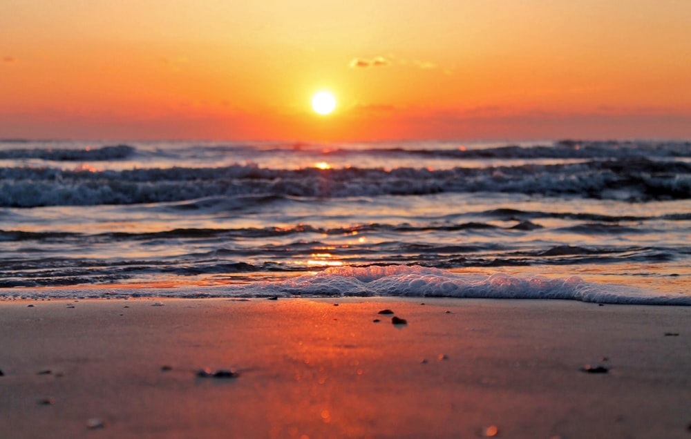 the sun is setting over the ocean on the beach