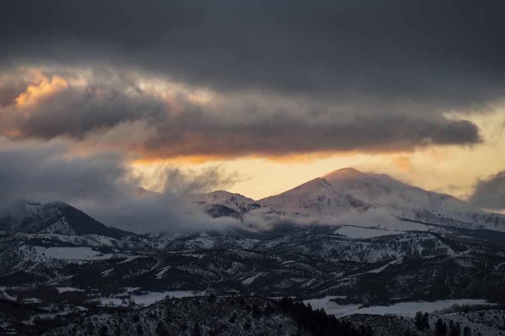 a mountain range covered in snow under a cloudy sky