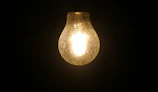 Soft glowing light bulb against a dark background symbolizing ideas coming soon.