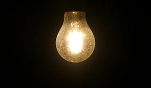 Soft glowing light bulb against a dark background symbolizing ideas coming soon.