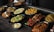A variety of Indian dishes are arranged on a dark rustic table. The spread includes colorful and flavorful looking food, such as curries, grilled vegetables, and rice, garnished with fresh herbs.