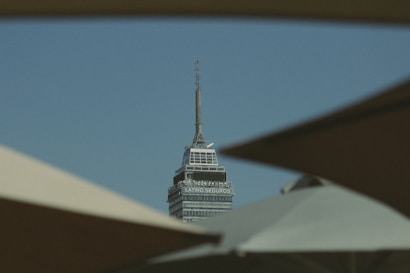 A tall, sharp-tipped skyscraper with the text 'Latino Seguros' is framed by dark shapes in the foreground against a clear blue sky.