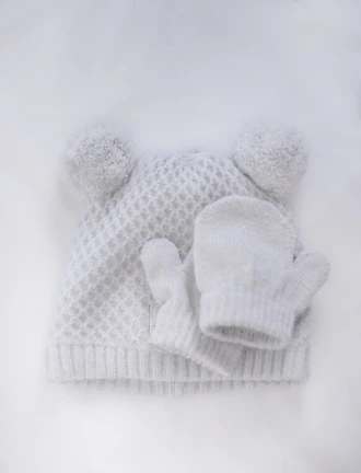 Flat lay of pastel pink crochet hats and mittens on a clean white surface.